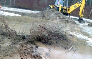 Akmenimis ir skudurais užkimšta pralaida paplovė kelią Vandens apsemtas ir paplautas kelias tapo neišvažiuojamas. A.Mekšėno nuotr.